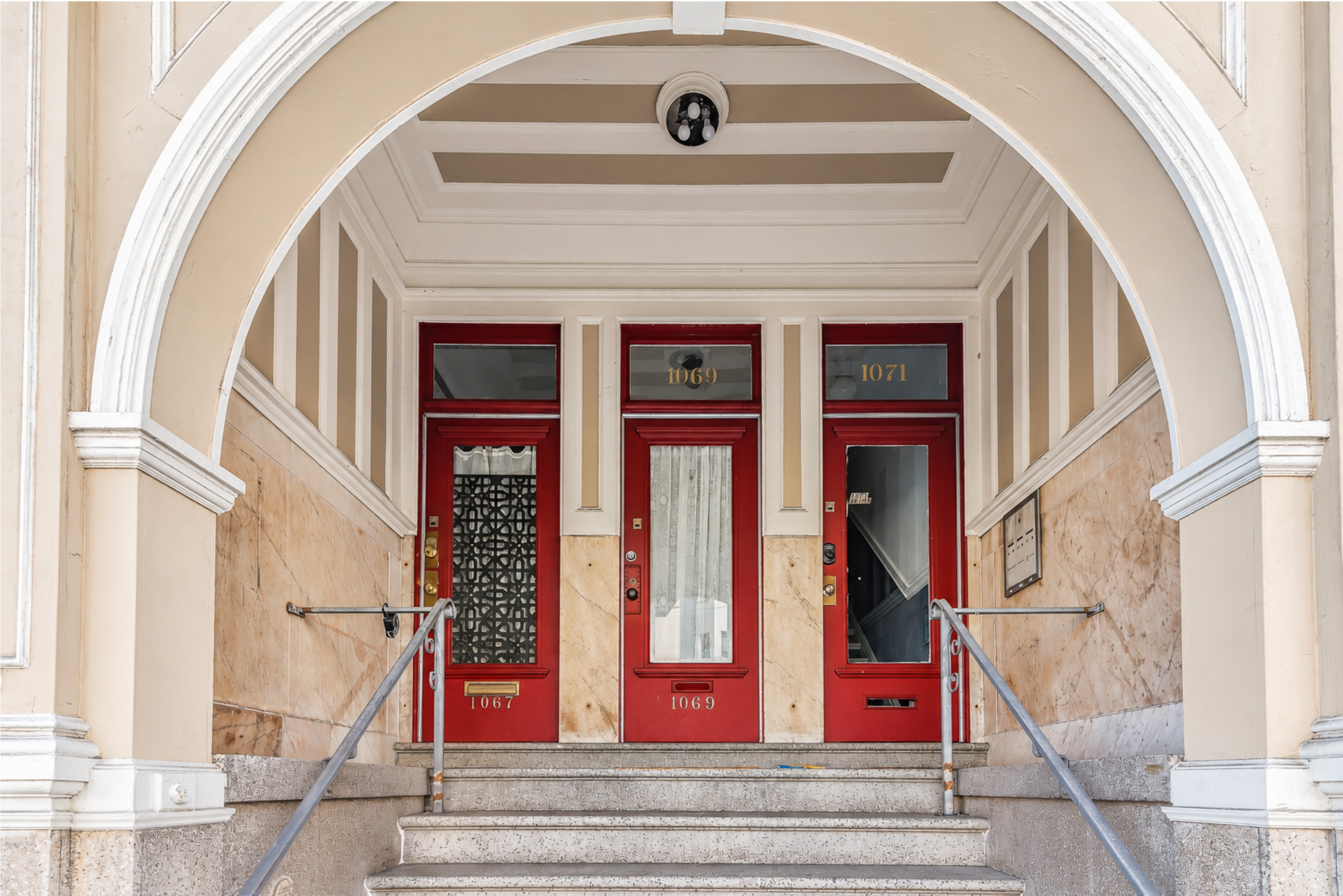 A red door with a glass window and a sign that says 1027 is on a building.